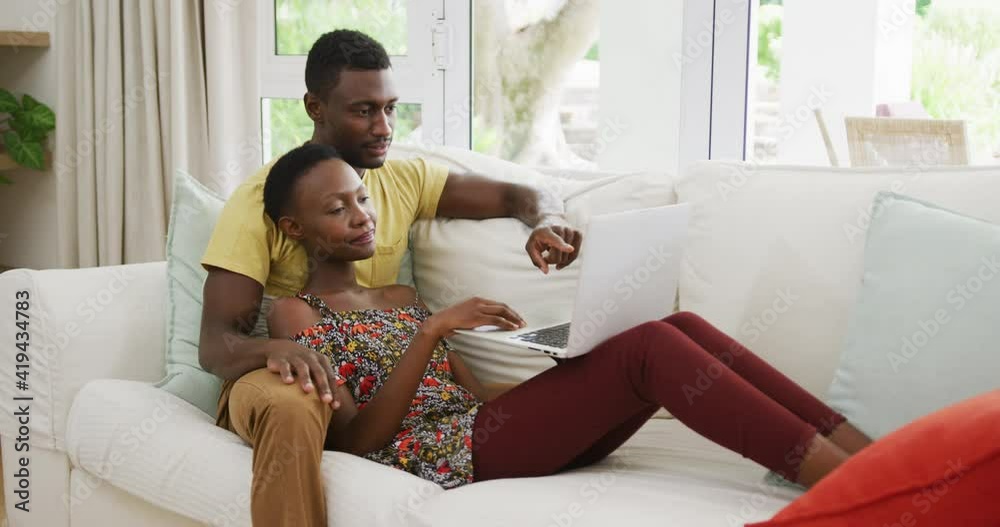 Happy african american couple on sofa embracing and talking looking at laptop Happy african american couple on sofa embracing and talking looking at laptop
