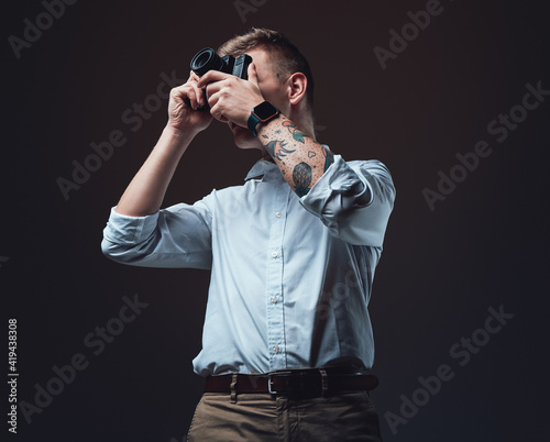 Stylish photographer with tattooed hand does shot using his photo camera. Professional portrait of a young man.