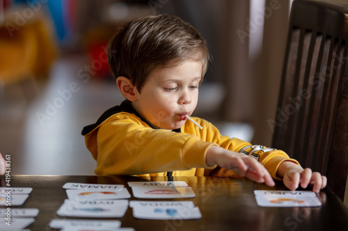 little boy learns words from cards under the ABA therapy program at home at the table photo
