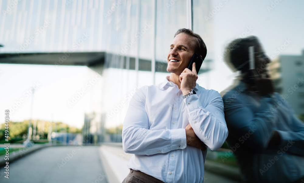 Cheerful businessman in white shirt smiling near urban building enjoying positive international conversation, happy male entrepreneur calling to friendly partner using roaming wireless connection Cheerful businessman in white shirt smiling near urban building enjoying positive international conversation, happy male entrepreneur calling to friendly partner using roaming wireless connection