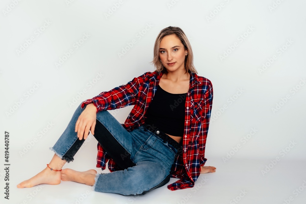 Young beautiful woman 20 years old wearing trendy black t-shirt, blue jeans and red check shirt. sexy female posing isolated near white wall in studio. 
