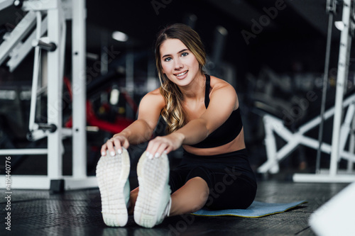 Attractive sports girl smiles and looks at the camera while stretching her body in the gym, lifestyle, healthy lifestyle