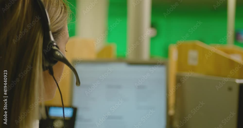Rear view female Call centre worker in headset talking on phone and answering of questions Slow motion . Service phone operator in earphones helping customers in business office . Blurred background