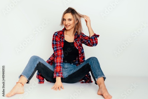 Young beautiful woman 20 years old wearing trendy black t-shirt, blue jeans and red check shirt. sexy female posing isolated near white wall in studio. 