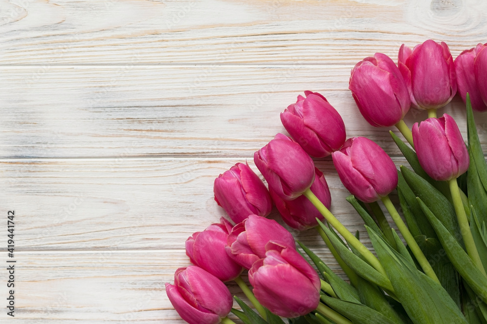 Wooden background with pink tulips, top view, space for text