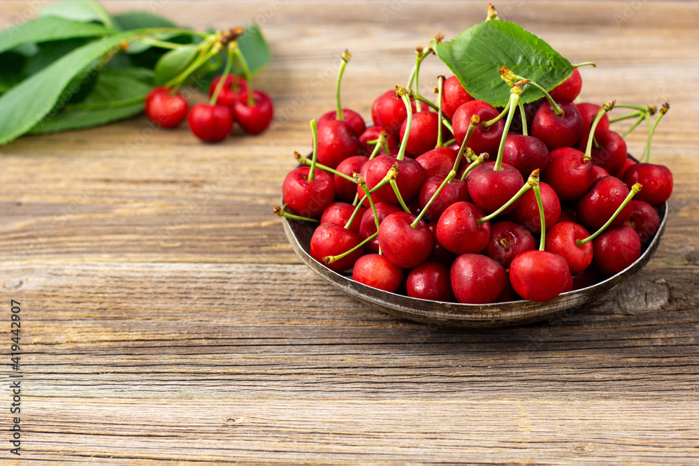 Ripe sweet cherries with green leaves in a metal plate on wooden background Ripe sweet cherries with green leaves in a metal plate on wooden background