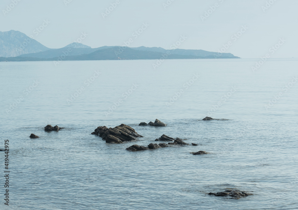 Fototapeta premium small rocks in the sea, beach view at dawn with hills on the horizon. Coasts of sardegna at dawn , olbia.
