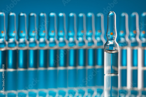 Medical glass ampoules with vaccine on a blue background. Shallow depth of field. Selective focus on one ampoule.
