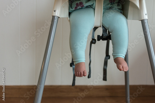 Baby legs dangling from high chair; baby wearing turquoise outfit with bare feet against white wood background photo