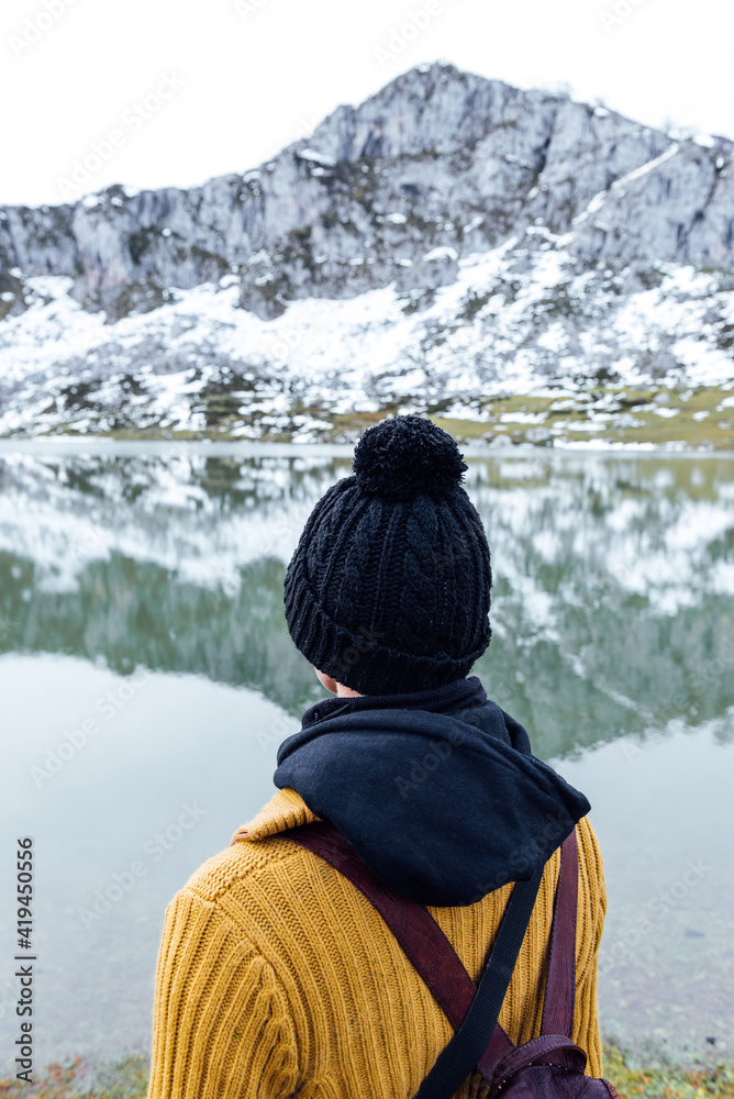 Back view of anonymous female with black hat standing on snowy rough highlands on lake shore Back view of anonymous female with black hat standing on snowy rough highlands on lake shore