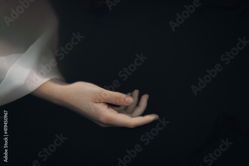 From above crop slim female hand in wet white translucent sleeve floating in dark lake water