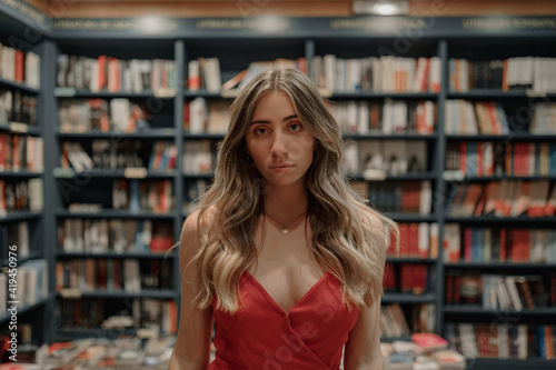 Elegant unemotional young woman in sundress standing against table with assorted textbooks in bookstore photo