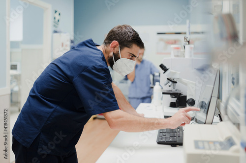 Side view of crop anonymous male medic in uniform and mask using microscope while working in lab photo