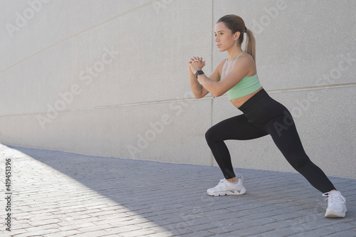 Side view of female athlete in sportswear doing lunge exercise while pumping hips during workout in summer in city