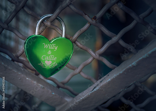 Close detail of shiny engraved green "love lock" - as worldwide tradition to resilient and everlasting love. Female's and male's name on the top. Selective focus.