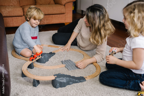 Young woman with little son and daughter playing with toy road and cars on carpet while spending free time together at home