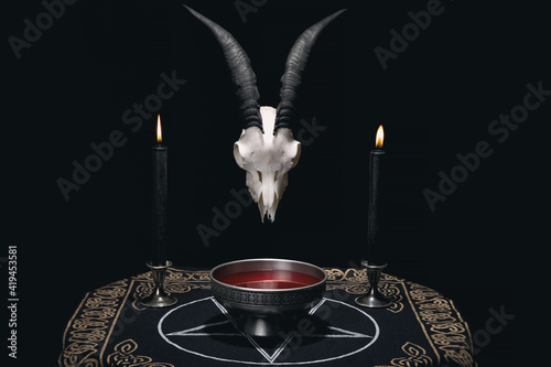 Altar for satanic rituals. Witchcraft composition with goat skull, pentagram cloth, candles and ritual bowl with blood. Occult and esoteric concept.
 photo
