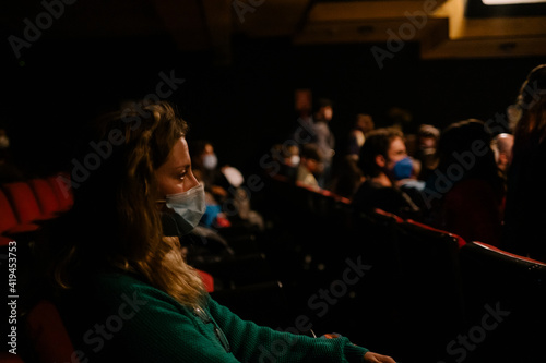 woman with mask watching a show in a theater keeping sanitary measures