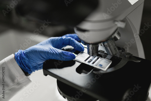Crop anonymous scientist in protective gloves putting sample under microscope lens while conducting chemical research in laboratory