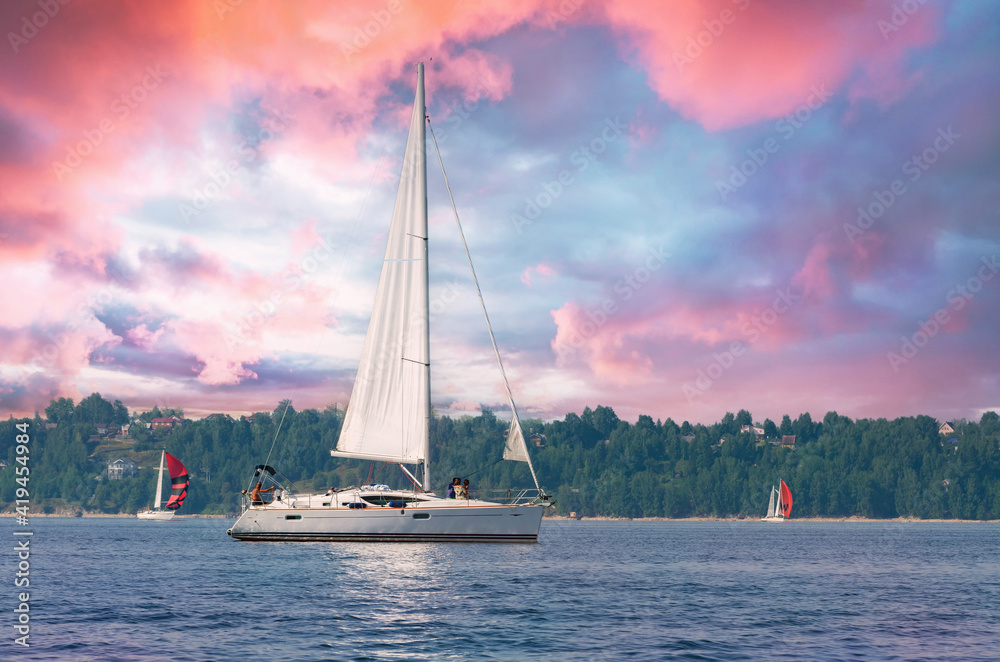 Obraz premium Sailing yachts sail under a beautiful evening sky with pink clouds.