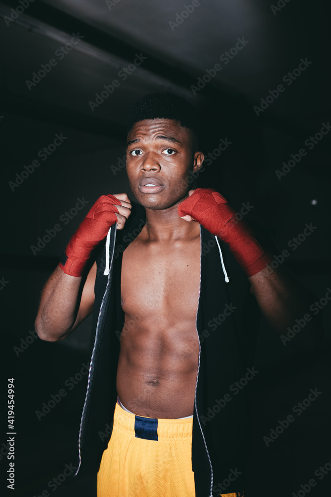 Young strong African American sportsman in boxing hand wraps working out and looking at camera in building Young strong African American sportsman in boxing hand wraps working out and looking at camera in building