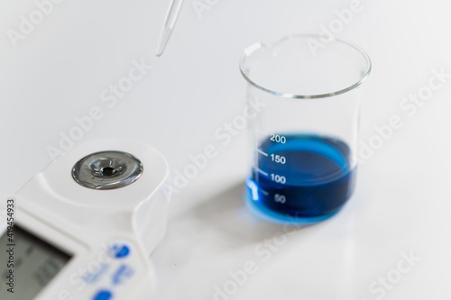 Closeup of glass container with blue chemical fluid and pipette placed near measuring equipment during medical research in lab photo