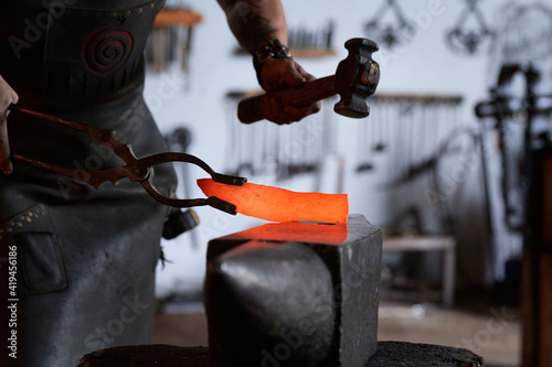 Side view of anonymous tattooed young male forger in apron heating metal in furnace while working in grungy smithy