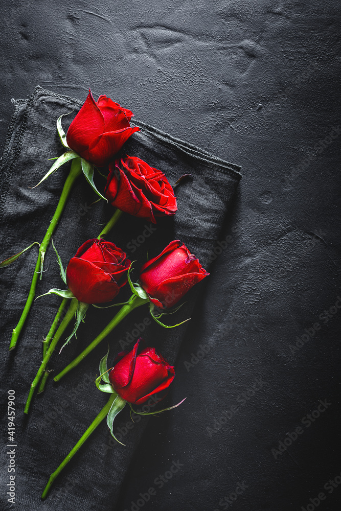 Top view composition of bright red blooming rose buds and petals scattered on black surface with cloth Top view composition of bright red blooming rose buds and petals scattered on black surface with cloth
