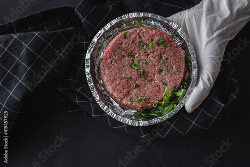 Top view of crop chef in glove holding takeaway foil container with minced beef cutlet and parsley
