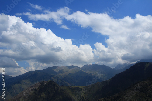 Above mountain ranges and peaks, low dense clouds on the Kok Zhailau plateau, blue sky, summer, sunny