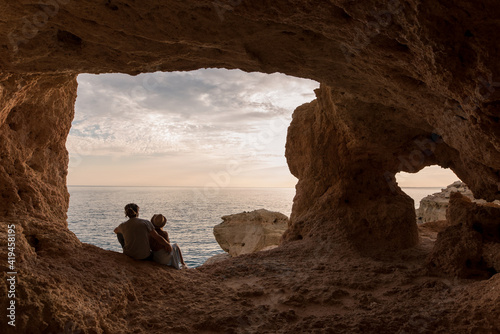 Baxk view of man and woman sitting in entrance of rocky cave near sea in Algar seco caves in Algarve, Portugal photo