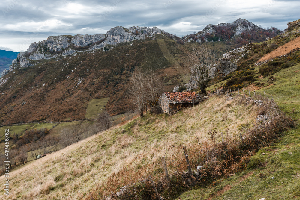 Weathered abandoned rural house near path on grassy slope in spacious mountainous terrain on overcast day in Asturias Spain