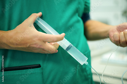 Crop anonymous doctor in medical uniform filling infusion drip with syringe while preparing intravenous procedure in hospital