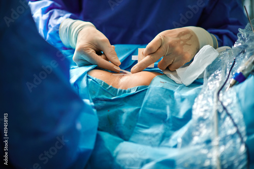 Crop unrecognizable surgeon attaching adhesive bandage on postoperative suture on breast of anonymous female patient after breast augmentation