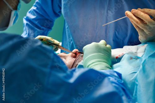 Crop unrecognizable plastic surgeons in gowns and gloves using tweezers while performing rhinoplasty operation in contemporary clinic