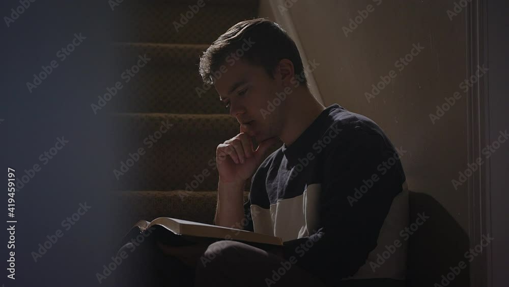 young man reading a bile on staircase