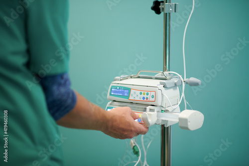 Side view of crop anonymous doctor in medical uniform controlling IV on modern infusion pump in operating room photo