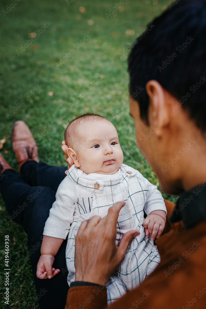 Crop unrecognizable loving dad communicating with adorable infant child while sitting on green lawn in park and enjoying summer day together Crop unrecognizable loving dad communicating with adorable infant child while sitting on green lawn in park and enjoying summer day together