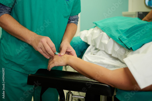 Crop unrecognizable medical assistants inserting intravenous catheter in hand on anonymous patient lying on couch in operating room photo