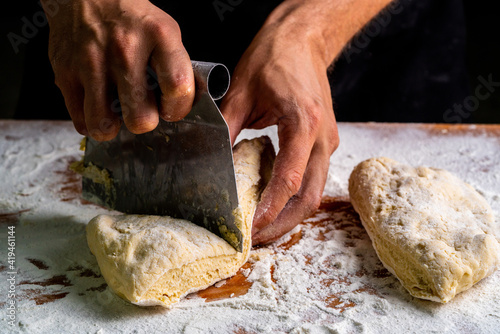 From above of man dividing raw bread dough with scraper on wooden table in baker photo