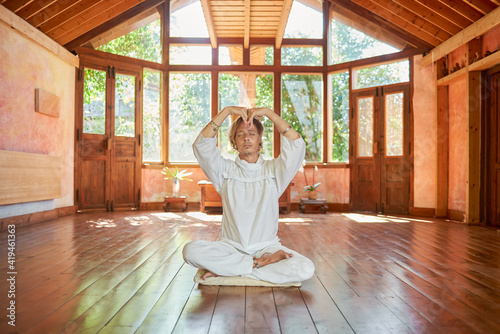 Young mindful male barefoot male sitting in lotus pose with eyes closed practicing yoga on floor near bowl gong and Buddha statuette photo