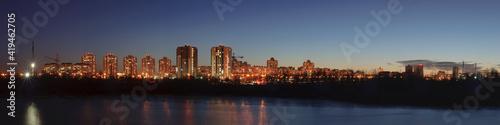 wide evening panoramic view of the modern residential quarter of the city in the coastal area with high-rise concrete buildings with light in the windows and bright street lighting © gluuker