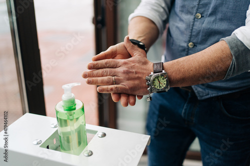 Crop anonymous male barber in wristwatch applying antibacterial gel on hands at work in beauty salon photo