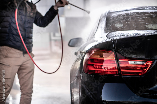 A man washes his luxury black sports car in a manual car wash.