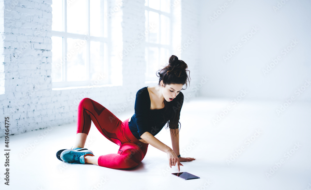 Fototapeta premium Shocked female athlete in sportive tracksuit using touch pad technology for checking online news, amazed fit girl watching online video webinar with aerobic exercises using digital tablet in gym