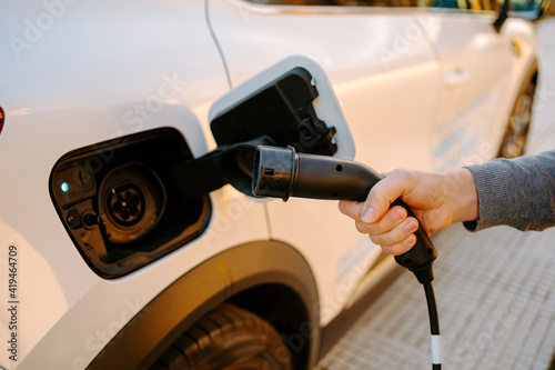 Side view of cropped unrecognizable man holding cable to plug and recharge electric modern car in petrol station in daytime