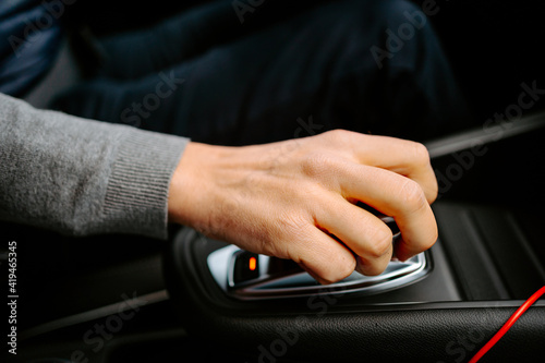 From above of crop unrecognizable male in casual clothes with hand on automatic gear driving modern car