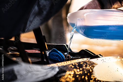 Pouring blue antifreeze liquid for washing car screen.
