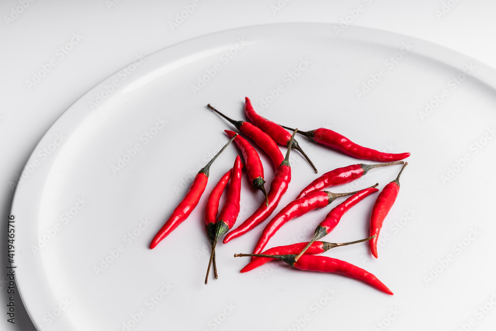 High angle composition of hot red chili peppers arranged around plate against white background High angle composition of hot red chili peppers arranged around plate against white background