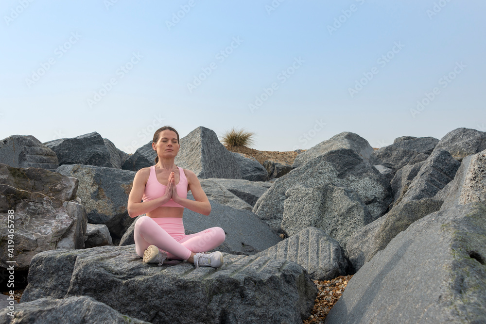 Woman sitting on rocks wearing pink sportswear practicing yoga and meditating.
